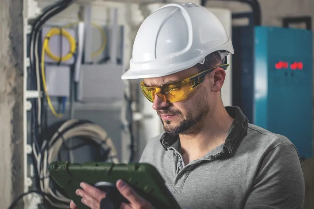 Man, an electrical technician working in a switchboard with fuses. Installation and connection of electrical equipment. Professional uses a tablet.