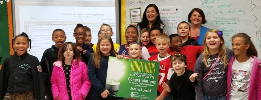 Image of elementary school kids and their teacher posing around a Bright Ideas poster.