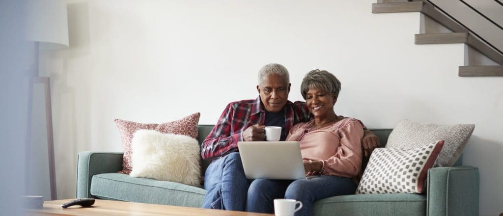Senior Couple Sitting On Sofa At Home Using Laptop