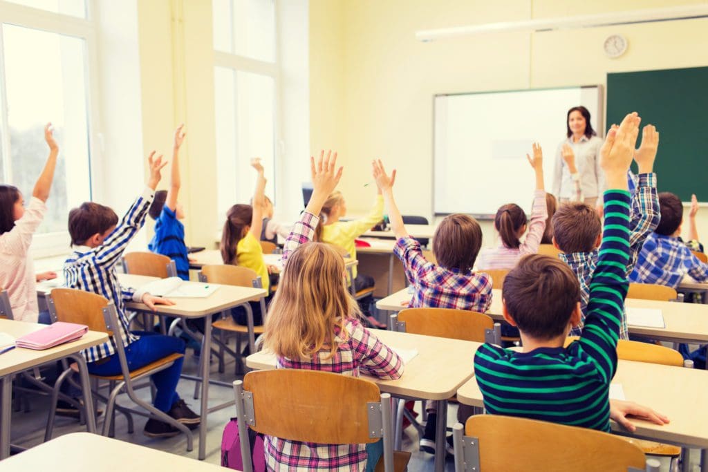 Kids in classroom with arms raised