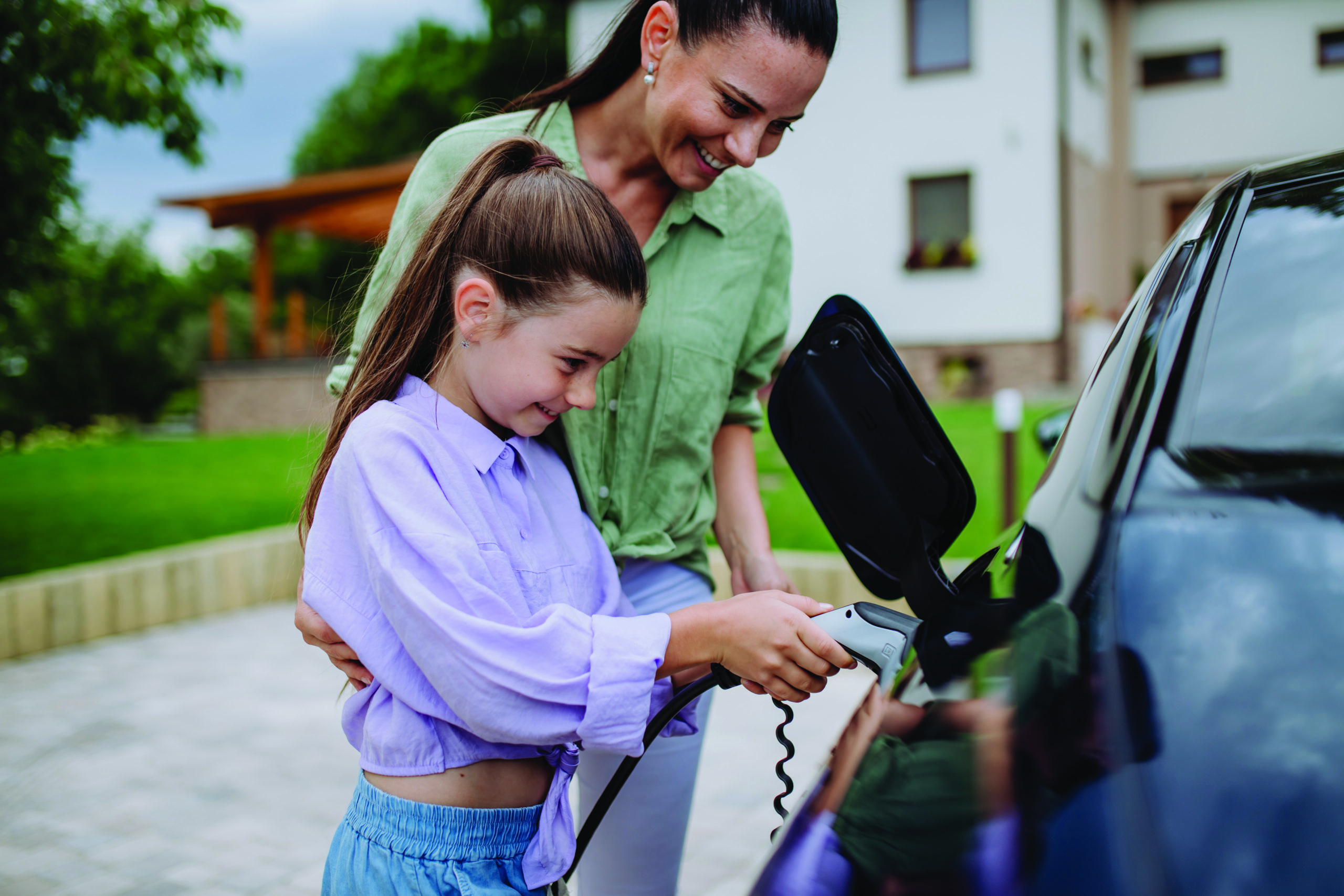 Mother showing daughter how to charge electric vehicle